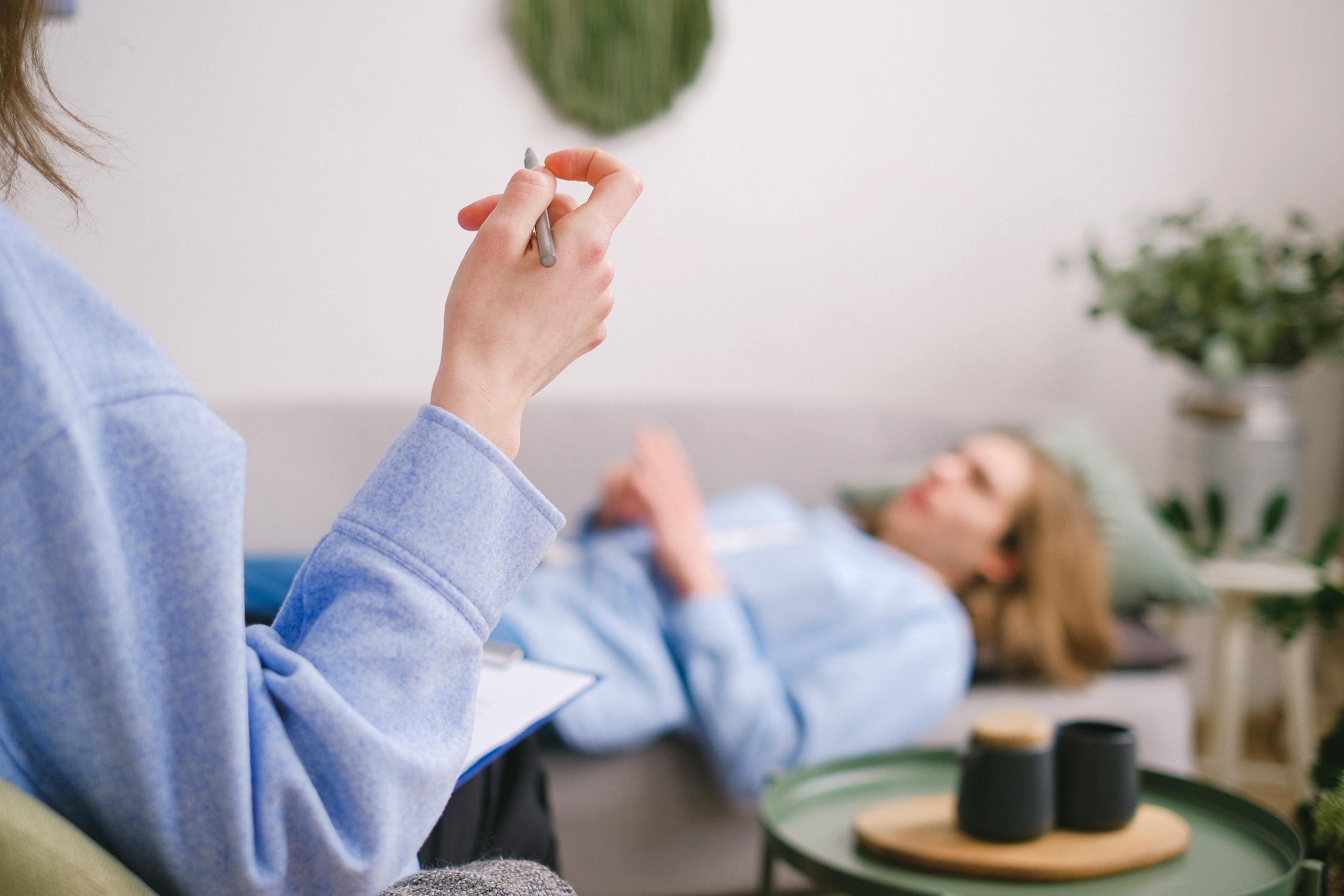 Therapist taking notes during a therapy session with a relaxed client lying on a couch.